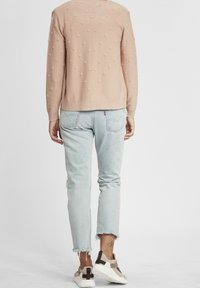 Light pink sweater with textured bobbles, paired with light blue distressed jeans. Sneakers feature a mix of beige and white with dark accents.