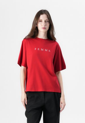 Červené bavlněné tričko s krátkým rukávem, s nápisem "FEMME" bílým písmem přes hruď. Spárováno s černými kalhotami.
