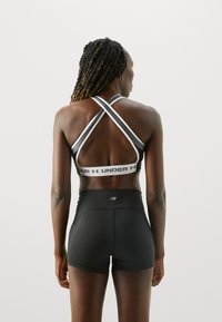 Svart sportsbh med kryssede stropper og logobånd, kombinert med høyt midje svarte shorts med en liten logodetalj.
