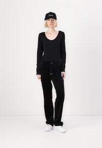 Svart langermet bodysuit og matchende svarte velour joggebukser med snøring. Hvit sneakers og en svart caps med "Juicy"-logo.