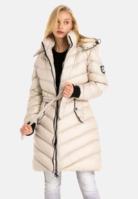 Beige Daunenjacke mit Zickzack-Steppung, hohem Kragen, Reißverschluss, verstellbare Kapuze und schwarzen Akzenten an den Manschetten und dem Reißverschluss.