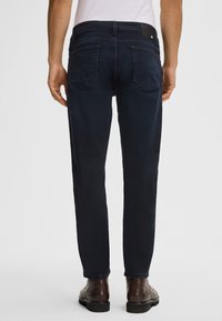 Jeans blu scuro con taglio dritto, dotati di tasche posteriori e di una toppa in pelle in vita, abbinati a scarpe in pelle marrone.