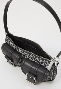 Sac à main noir avec fermeture éclair. Présente deux poches arrondies à l'avant, des accents métalliques et un motif de logo graphique en gris et noir.