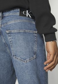 Calvin Klein blå jeans i denim med en svart logotypetikett vid midjebandet, med en klassisk design med fem fickor och blekt textur.