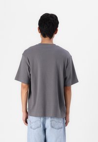 Tricou cu mânecă scurtă, guler rotund, din bumbac, într-o nuanță solidă de gri, cu o croială relaxată și un tiv drept în talie.