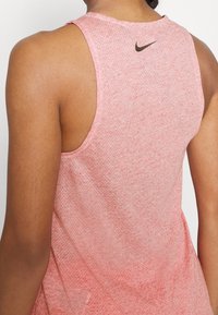 Nike sporttanktop in lichtroze, met een ademende textuur, brede armsgaten en een zwart logo-accent op de achterkant van de hals.