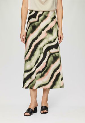 Donna che indossa una gonna midi con motivi astratti verdi, rosa e neri a ondulazioni, abbinata a un top beige e a dei sandalini con il tacco aperti neri.
