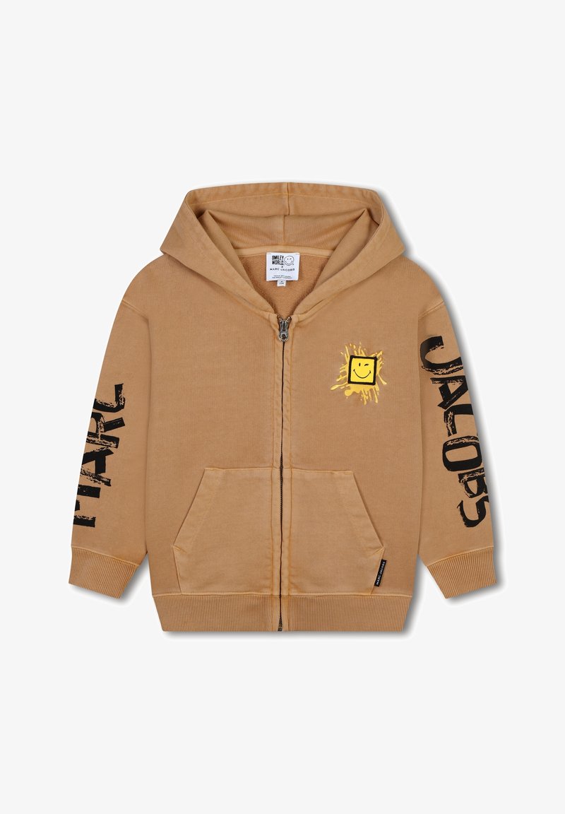 Haut à zip beige en coton doux, avec une poche avant, un grand texte noir "JACOBS" sur une manche, et un graphique de smiley jaune sur la poitrine.