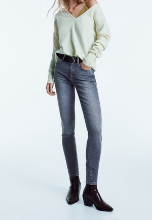 Lichtgroene oversized trui met V-hals, gecombineerd met slim-fit grijze jeans. Zwarte riem en enkellaarsjes met een spitse neus en chunky hak.