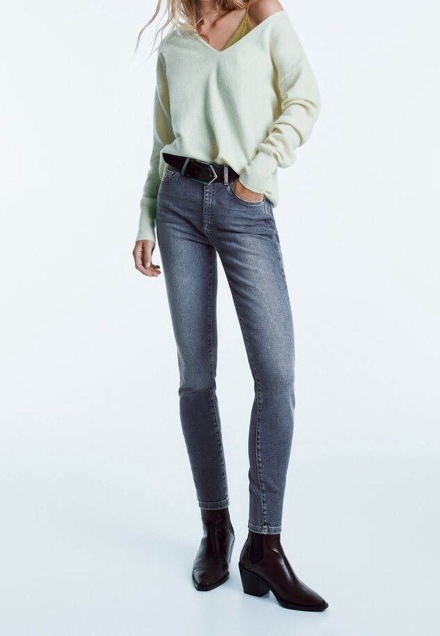 Lichtgroene oversized trui met V-hals, gecombineerd met slim-fit grijze jeans. Zwarte riem en enkellaarsjes met een spitse neus en chunky hak.