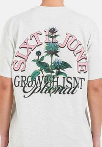 Camiseta de color gris claro con un gráfico floral y el texto "SIXTH JUNE GROWTH ISN'T OPTIONAL" en rosa y negro, exhibiendo colores y detalles vibrantes.