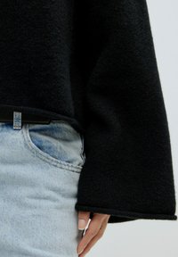 Zwart gebreid sweater met een omgeslagen, brede mouwontwerp, gecombineerd met lichtblauwe denim jeans met een zichtbare zak en een lichte wassering.