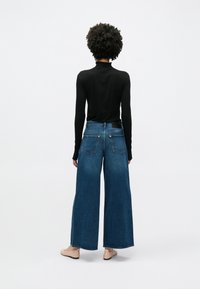 Φαρδιά μπλε τζιν παντελόνια με ψηλή μέση, σε συνδυασμό με μαύρο μακρυμάνικο τοπ. Διαθέτουν τσέπες στο πίσω μέρος και καθαρό τελείωμα.