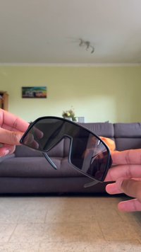 Mustad suured prillid, millel on geomeetriline disain, tumedad objektiivid ja kitsad käed, mida peetakse kahe käe vahel. Matt viimistlus, minimaalne riistvara.