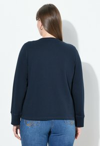 Felpa a maniche lunghe blu navy con scollo rotondo e polsini a coste. Realizzata in materiale morbido, presenta una texture liscia e una vestibilità comoda.