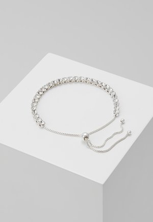 Bracelet ajustable en argent avec pierres précieuses carrées transparentes et fermoir coulissant sur un bloc d'exposition blanc.