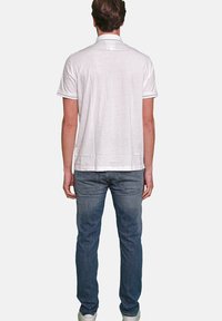 Weißes Poloshirt mit kurzen Ärmeln und Kragen, das eine subtile Textur aufweist. Getragen mit blauen Jeans und weißen Sneakern. Ansicht von hinten.