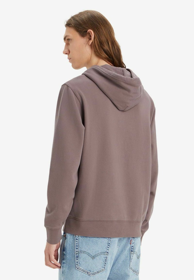 Sudadera gris con capucha ajustable, con una textura suave y puños acanalados, combinada con jeans de mezclilla azul claro.