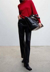 Un pull rouge ample associé à un pantalon en cuir noir taille haute. Tenant un sac fourre-tout noir brillant. Bottes noires à bout carré.