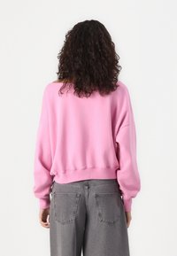 Sweatshirt rosa oversize con maniche lunghe e orlo a coste, abbinato a jeans grigi a vita alta con tasche posteriori.