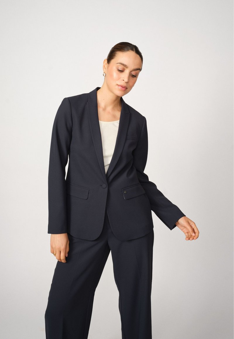 Námořnický blazer s přiléhavým střihem, zapínání na jeden knoflík, klopové límce a dvě přední kapsy, zkombinovaný s odpovídajícími kalhotami.