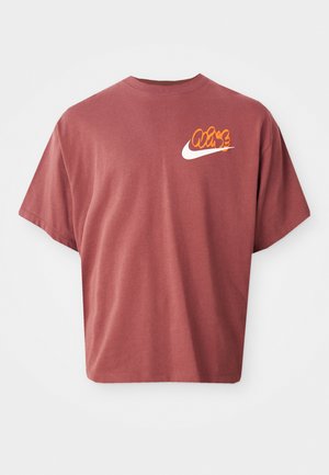 T-shirt in cotone color mogano con vestibilità rilassata, caratterizzato da un logo Nike bianco e un design grafico arancione sull'area sinistra del petto.