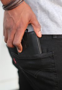 Black leather wallet being pulled from a back pocket, with a smooth texture and minimalistic design, held by a hand wearing a brown bracelet.