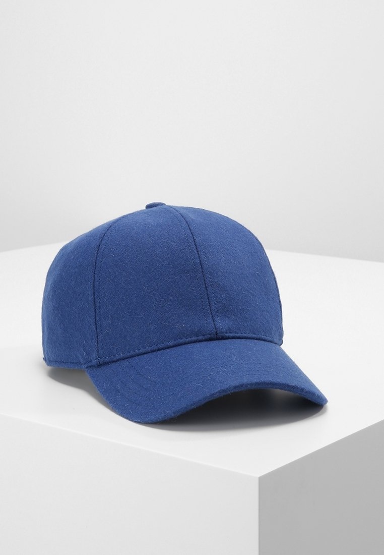 Casquette de baseball en tissu bleu avec une couronne arrondie et une visière courbée reposant sur une surface blanche sur fond uni.