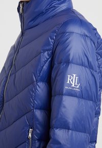 Dunjacka i klarblått, tillverkad av glänsande nylon, med hög krage, dragkedjestängning och diagonala sömmar med en Ralph Lauren-logotyp.