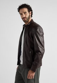 Brun läderjacka med ståkrage, dragkedja fram och sidofickor. Slät textur, figursydd design och dämpad färgpalett.