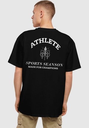 Sort T-shirt med hvid tekst på ryggen, der står "ATHLETE," med et grafisk design ovenfor. Korte ærmer og en afslappet pasform.