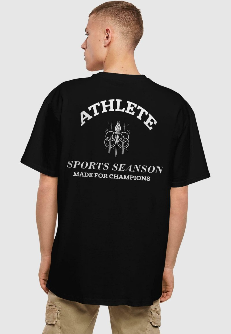Juodas marškinėlis su balta užrašu ant nugaros "ATHLETE", virš jo esantį grafikos dizainą. Trumpomis rankovėmis ir laisvu kirpimu.