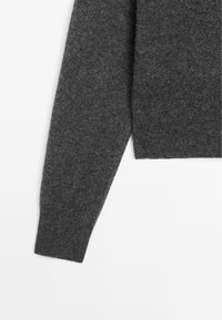 Manica di maglione grigio scuro realizzata in un tessuto morbido con una texture liscia e polsino aderente. Design semplice e minimalista senza motivi visibili.