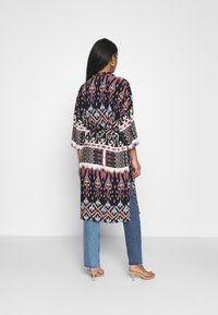 Czarny kimono w wzory z czerwonymi, niebieskimi i białymi geometrycznymi wzorami, luźnymi rękawami i paskiem w talii, sparowane z dżinsami.