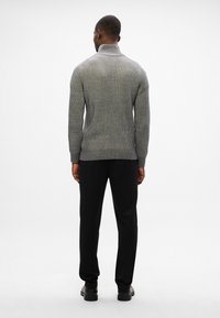 Suéter gris de canalé con cuello alto, combinado con pantalones negros. El suéter presenta una tela texturizada y una silueta ajustada.