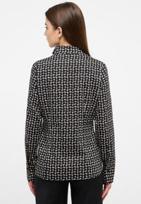 Damenbluse mit einem schwarzen und beigen Muster, langen Ärmeln, Kragen-Design, glatter Textur, tailliertem Rücken und leicht geschwungenem Saum.