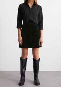 Chemise noire à manches longues associée à une jupe mini en velours côtelé noire et des bottes en cuir noir jusqu'aux genoux. Textures lisses, coupe ajustée.