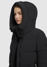 Fekete puffdzseki nagy kapucnival, cipzáras záródással, steppelt textúrájú, oldalsó zsebekkel és logós részlettel az ujjon.