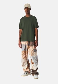 Zelené bavlnené tričko s krátkymi rukávmi v kombinácii s viacfarebnými cargo nohavicami so abstraktnými vzormi. Biely tenisky dotvárajú outfit.