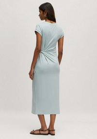 Lichtblauwe jurk tot de knie met een twist-detail op de achterkant, korte mouwen en gemaakt van een glad, rekbaar materiaal.