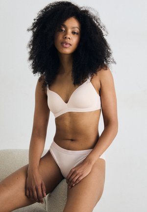 Lichtroze draadloze beha met een zachte textuur en driehoekige cups, gecombineerd met bijpassende low-rise slip, die een minimalistisch ontwerp laat zien.