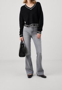 Pull noir court avec bordure en V blanche et ourlet marqué d'une marque, associé à un jean évasé gris clair et un petit sac à main noir texturé.