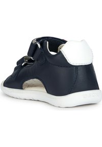 Sandalo in pelle blu navy con tacco bianco, dettagli a taglio, doppi cinturini in Velcro e suola in gomma bianca con texture. Logo del marchio sulla suola.