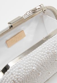 Bolso de mano blanco con una superficie texturizada de pequeñas perlas. Cuenta con un marco y un cierre metálico plateado, y un interior de satén suave.