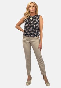 Beżowe dopasowane spodnie i czarne bezrękawnik z kwiatowym wzorem, oraz metaliczne koturny. Top ma biało-różowe kwiatowe wzory i gładką tkaninę.