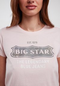 Rožinė medvilninė marškinė su išblukusiu pilku piešiniu "BIG STAR" ir "LEGENDINIAIS MĖLYNAIS DŽINSAIS", apvali iškirptė, trumpomis rankovėmis.