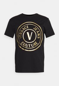 Schwarzes Baumwoll-T-Shirt mit einem großen goldenen Folien-Logo in Kreisform, auf dem der Text "VERSACE JEANS COUTURE" und ein zentrales "V"-Design zu sehen sind.