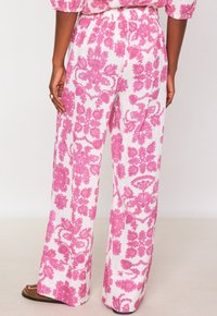 Pantalon large en tissu léger avec un motif floral rose sur fond blanc. Taille élastique et coupe décontractée. Ourlet plat.