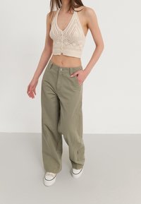 Haut court en maille beige avec un col en V et des détails à boutons, associé à un pantalon cargo ample vert olive avec poches latérales et coupe droite.