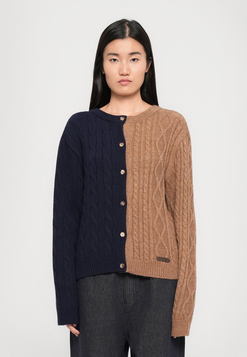 Käsinvärvad cardigan med navy och beige färger, knappstängning och kontrasterande texturerade mönster på varje sida. Mjuk, varm stickad material.